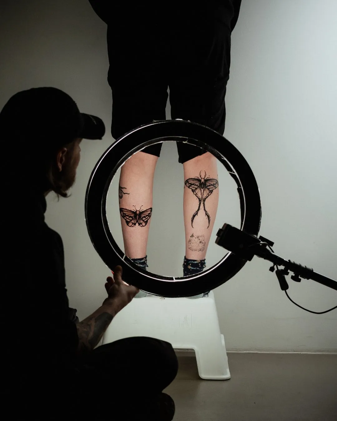 Matching moth tattoos on a client's calves, lit by a ring light at GON Berlin