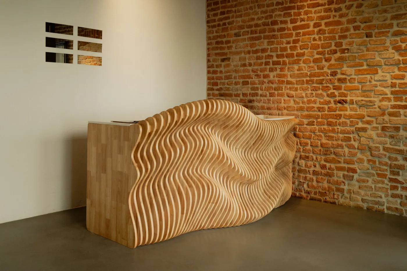 Curved parametric oak reception desk against exposed brick at GON Berlin