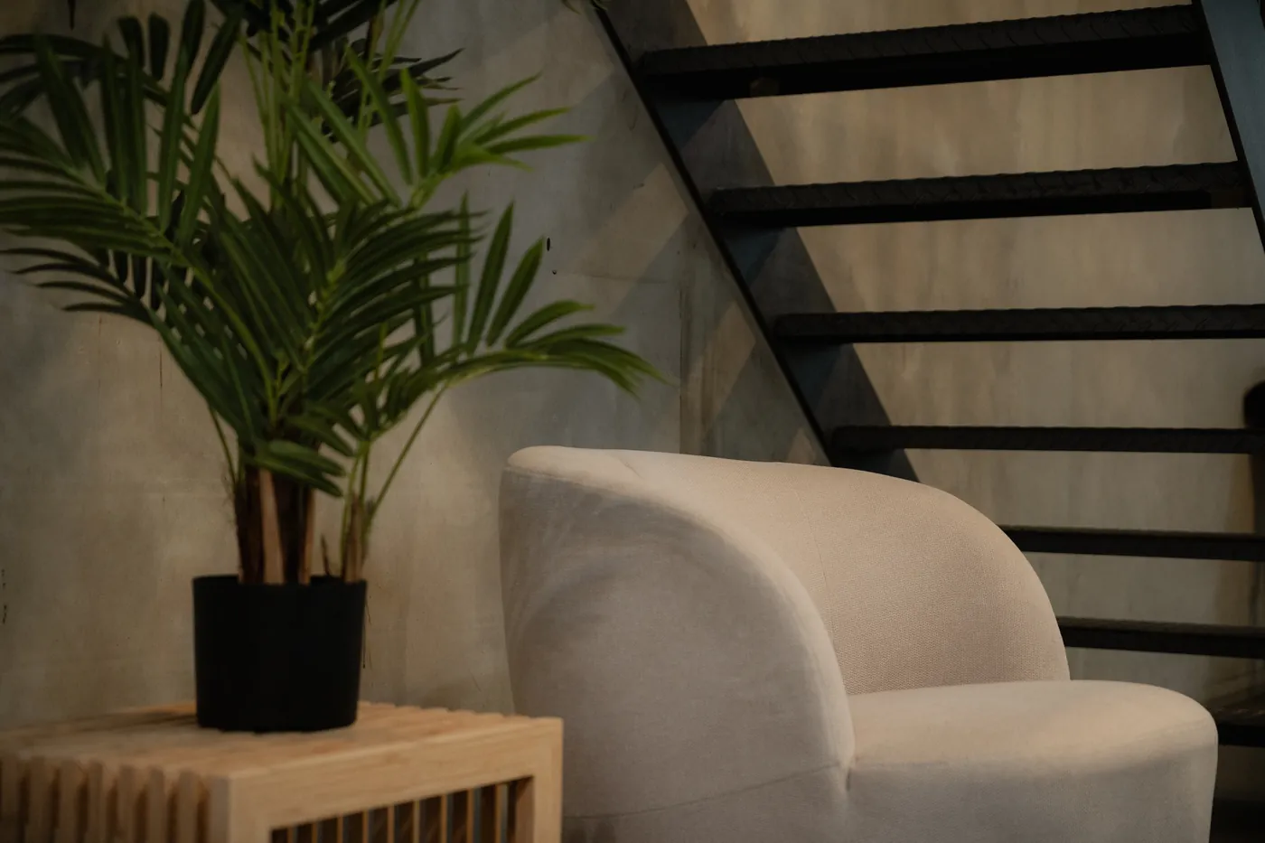 Cream bouclé armchair beside a potted palm and the black steel staircase at GON Berlin