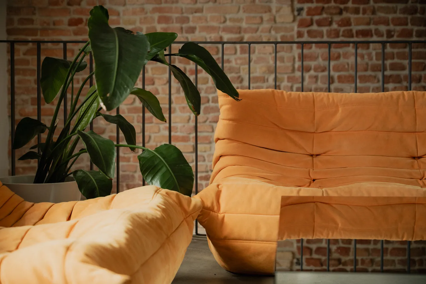 Orange Togo sofa and a tall plant beside an exposed brick wall in the GON Berlin lounge